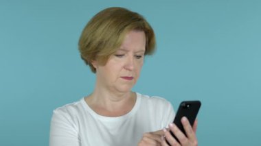 Mavi arka planda Izole Smartphone kullanırken şaşırttı yaşlı kadın heyecanlı