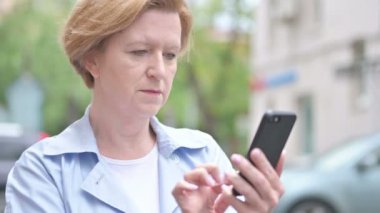Eski kadın tarama Smartphone ayakta açık