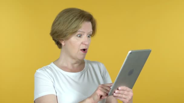 Стара жінка задоволена успіхом під час використання планшета ізольовано на жовтому тлі — стокове відео