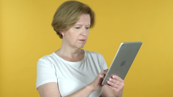 Mujer vieja en shock mientras usa la tableta aislada sobre fondo amarillo — Vídeos de Stock