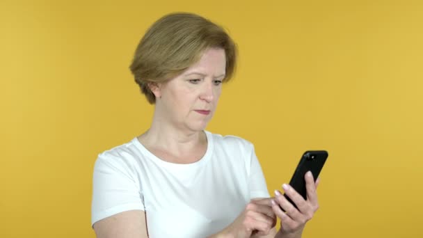 Mulher velha reagindo à perda e usando Smartphone isolado em fundo amarelo — Vídeo de Stock