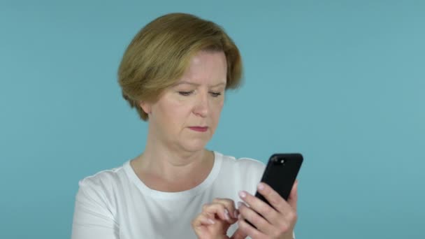 Vecchia donna eccitata per il successo durante l'utilizzo di smartphone isolato su sfondo blu — Video Stock