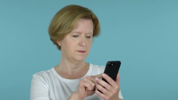 Старуха просматривает смартфон изолированный на голубом фоне — стоковое видео