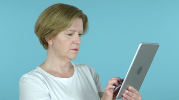 Alte Frau freut sich auf Erfolg, während sie Tablette isoliert auf blauem Hintergrund verwendet — Stockvideo