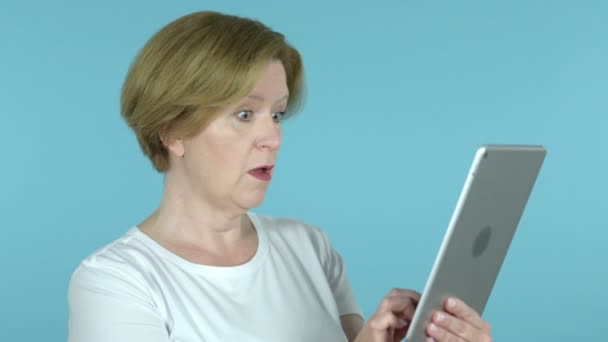 Gammal kvinna i chock när du använder tabletten isolerad på blå bakgrund — Stockvideo