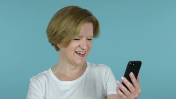 Online video chat via smartphone av gammal kvinna, blå bakgrund — Stockvideo