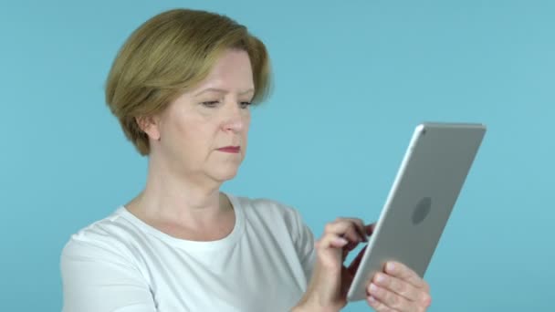 Alte Frau blättert auf Tablet, blauer Hintergrund — Stockvideo