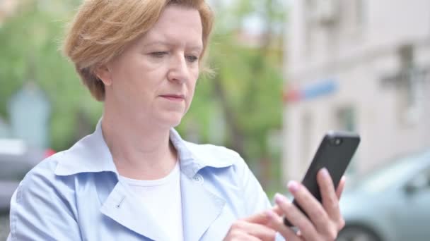 Utomhus gammal kvinna upphetsad för framgång när du använder smartphone — Stockvideo