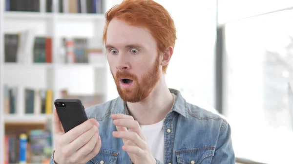 Jonge Redhead man geschokt door resultaten op de telefoon — Stockfoto