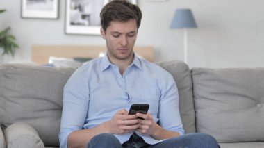 Kanepe üzerinde rahatlatıcı iken Smartphone kullanarak genç adam