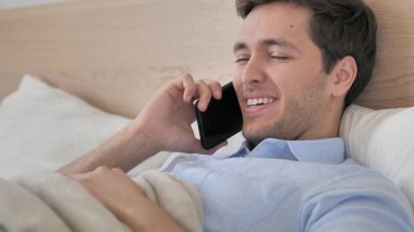 Yatakta telefonda konuşan rahatlatıcı genç adam