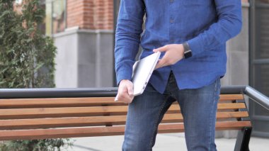 Genç adam geliyor ve laptop kullanmak için Bench oturuyor