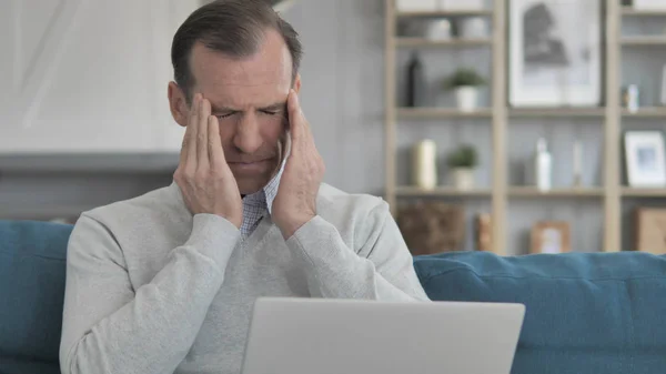 Middle Aged człowiek z ból głowy praca na laptop podczas siedzący na tapczan — Zdjęcie stockowe