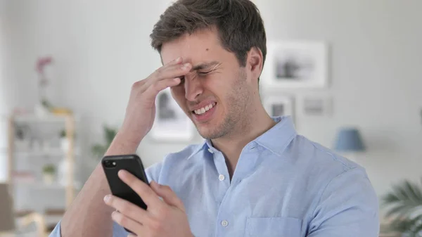 Pohledný mladý muž šokovaný výsledky v telefonu — Stock fotografie