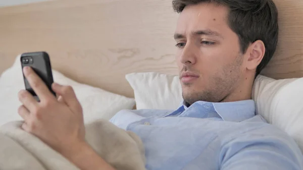 Fiatal férfi használ okostelefon az ágyban — Stock Fotó
