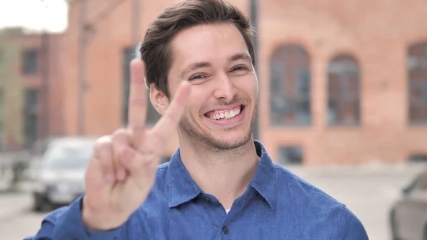 Siegeszeichen von positivem jungen Mann im Freien — Stockfoto