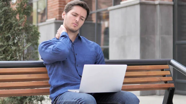 Sentado ao ar livre, jovem com dor no pescoço trabalhando no laptop — Fotografia de Stock