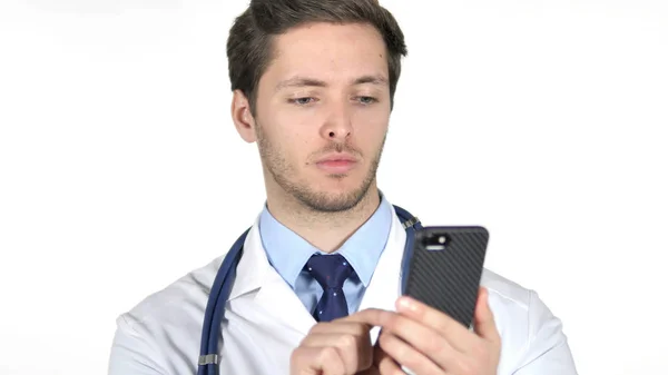 Молодой доктор просматривает смартфон, белый фон — стоковое фото