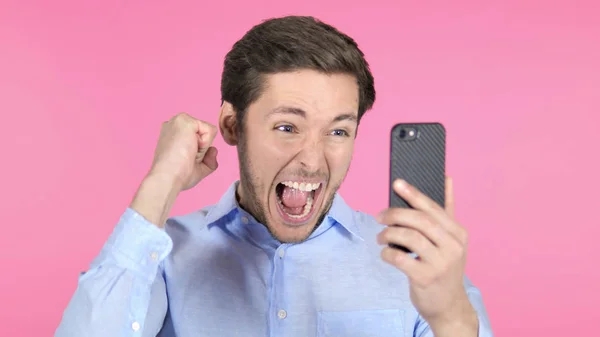 Junger Mann feiert Erfolg mit Smartphone auf rosa Hintergrund — Stockfoto