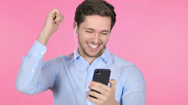 Tanzender junger Mann hört Musik auf Smartphone auf rosa Hintergrund — Stockfoto