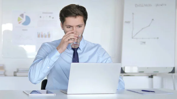 Fiatal üzletember ivóvíz ivóvizet, miközben dolgozik laptop — Stock Fotó