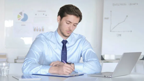 Jeune homme d'affaires réfléchi écrivant au bureau — Photo