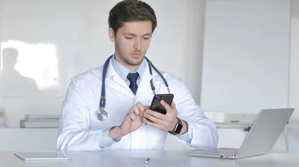 クリニックでスマートフォンを閲覧する若い医師 — ストック写真