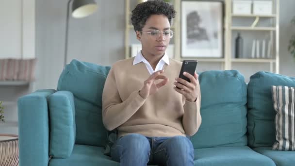 Chica alegre usando el teléfono mientras está sentado en el sofá — Vídeo de stock