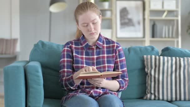 Jonge vrouw zittend op de Bank en lezen — Stockvideo