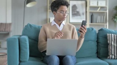 Genç Afrikalı Kız Kanepede telefon ve dizüstü bilgisayar ile çalışıyor