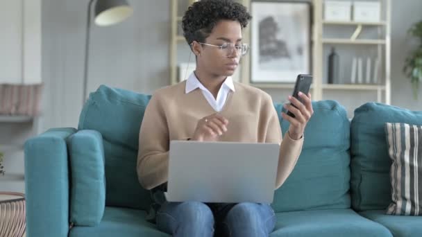 Ung afrikansk flicka som arbetar med telefon och laptop på soffan — Stockvideo