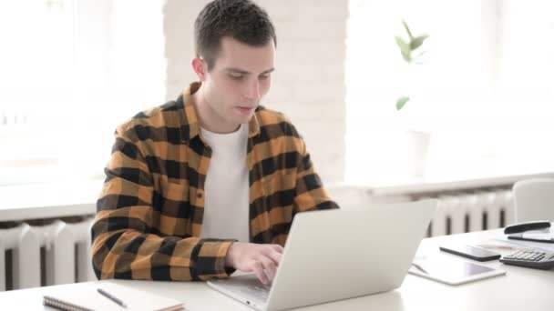 Случайный молодой человек с болью в шее работает над ноутбуком — стоковое видео