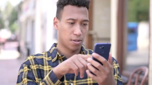 スマートフォンでオンライン成功を祝うアフリカ人男性,屋外 — ストック動画