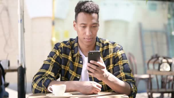 Νέος Αφρικανός άνθρωπος χρησιμοποιώντας smartphone, υπαίθριο Cafe — Αρχείο Βίντεο