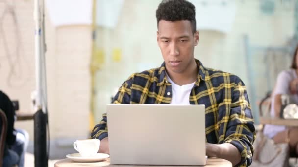 Молодой африканский человек разочарован результатами на ноутбуке, в открытом кафе — стоковое видео