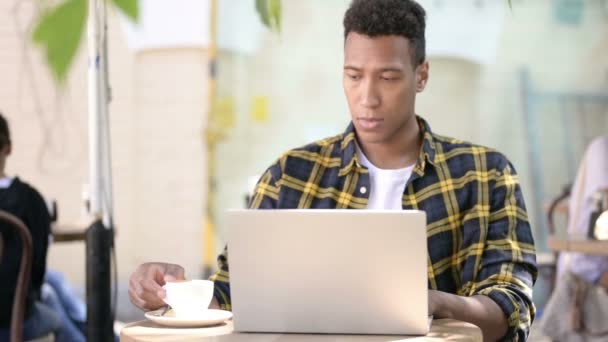 Hombre joven africano bebiendo café y trabajando en el ordenador portátil, Café al aire libre — Vídeo de stock
