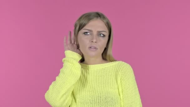 Удивлённая молодая девушка пытается слушать тайну, розовый фон — стоковое видео