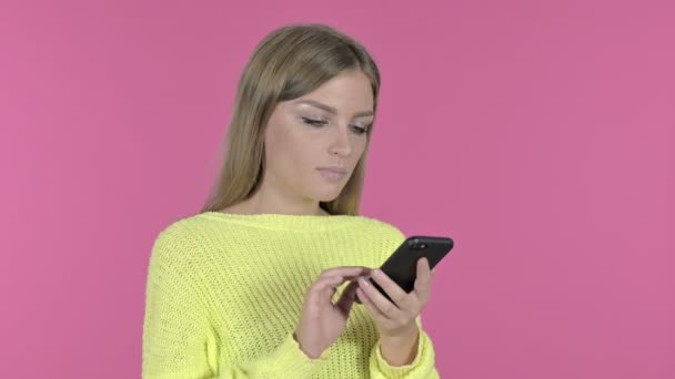 Opgewonden meisje cheering succes tijdens het gebruik van smartphone, roze achtergrond — Stockvideo