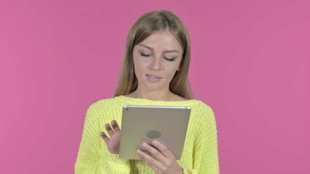 Молода дівчина використовує планшет і посміхається, рожевий фон — стокове відео