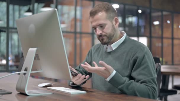 Boos Man krijgen Call op mobiele telefoon tijdens het werken op de computer — Stockvideo