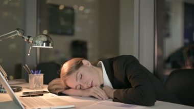 Genç iş kadını geceleri ofis masasında kestiriyor.