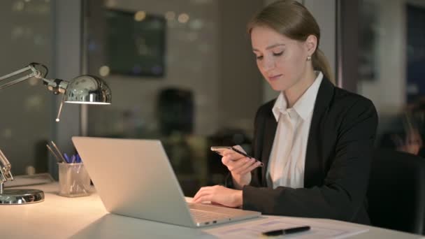 Jonge zakenvrouw met behulp van mobiele telefoon op Office Desk 's nachts — Stockvideo