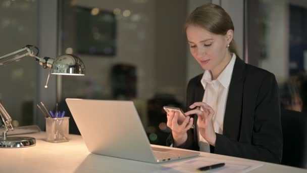 Erfolgreiche Geschäftsfrau scrollt nachts mit Handy im Büro — Stockvideo