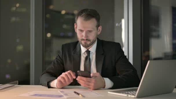 Závažný podnikatel používající mobilní telefon v kanceláři v noci — Stock video