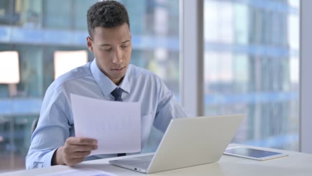 Афроамериканский бизнесмен читает документы в офисе — стоковое видео