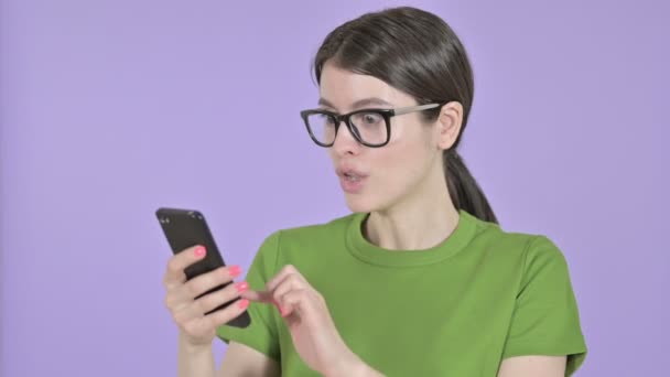 Mujer joven sorprendida usando el teléfono celular sobre fondo rosa — Vídeos de Stock