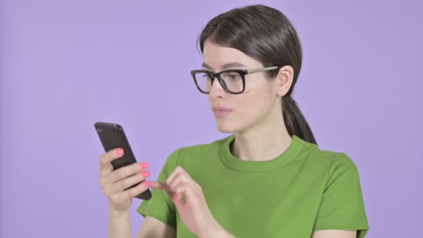 Mujer joven conmocionada usando el teléfono celular sobre fondo rosa — Vídeos de Stock