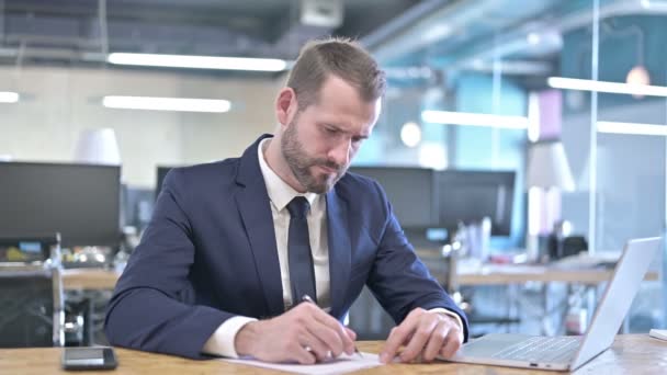 Wütender junger Geschäftsmann schreibt Dokumente auf Schreibtisch — Stockvideo