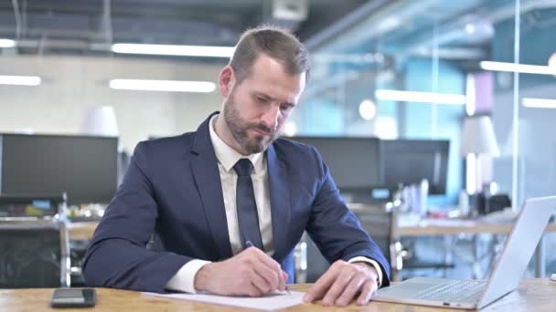 Молодой бизнесмен пишет документы на рабочем столе — стоковое видео