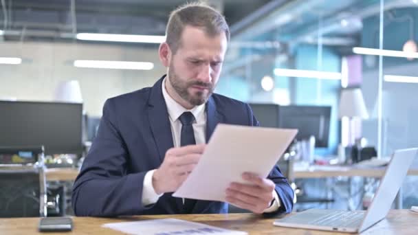 Feldúlt fiatal üzletember olvassa a dokumentumokat a hivatalban — Stock videók